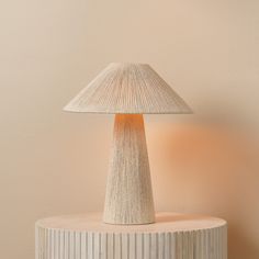 a white lamp sitting on top of a wooden table next to a light pink wall