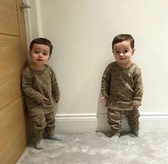 two young boys standing next to each other in matching pajamas and pants, both looking at the camera