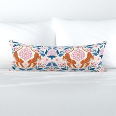 a white bed topped with two pillows and a pillow covered in an orange tiger pattern