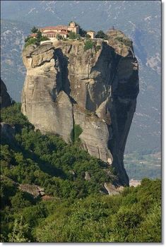 a house on top of a rock in the middle of mountains with trees around it