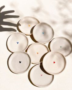 six white plates with hearts on them are arranged in the shape of a hand and shadow