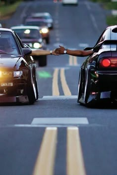 two cars driving down the road with one being pushed over by someone's arm