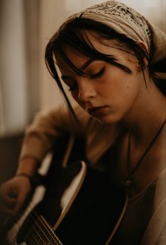 a woman is playing an acoustic guitar with her eyes closed and head tilted to the side