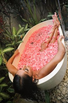 a woman laying down in a bathtub filled with pink flowers next to greenery