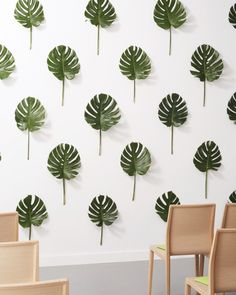 the wall is decorated with green leaves and has two chairs in front of it that are facing each other