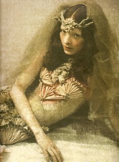 a woman with long hair sitting on a bed wearing a headdress and veil