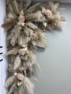 an arrangement of dried flowers and feathers hangs on the wall in front of a door