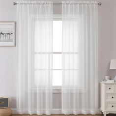 a white curtain hanging on the side of a window next to a dresser and lamp