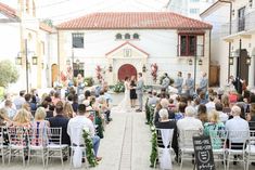 an outdoor wedding ceremony in front of a building with lots of people sitting on chairs