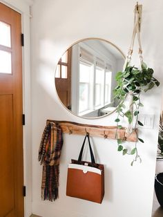 a mirror hanging on the wall next to a purse and coat rack with a plant