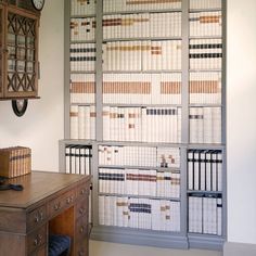 a room with a desk, chair and bookshelf that has many papers on it