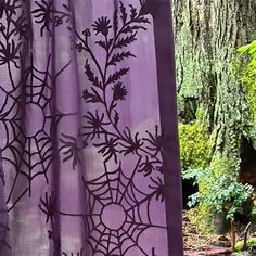 a purple shower curtain with black spider webs on it in front of a tree