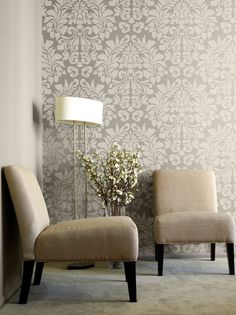 two chairs in front of a wall with a lamp next to it and a vase on the floor