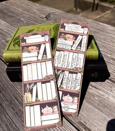 two bookmarks sitting on top of a wooden table next to a green tray filled with books