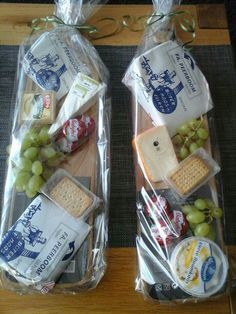 two breads with cheese, grapes and crackers wrapped in cellophane to look like they are sitting on a table