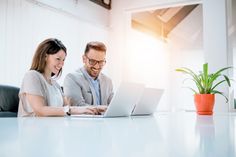 a man and woman sitting at a table looking at a laptop computer while they look at the screen