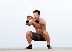 a shirtless man squatting on the beach with his hands in the air while wearing black shorts