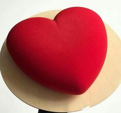 a large red heart sitting on top of a white and beige plate with a black handle