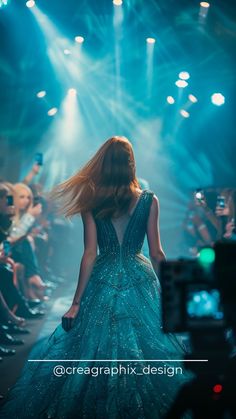 a woman in a blue dress walking down the runway at a fashion show with lights behind her