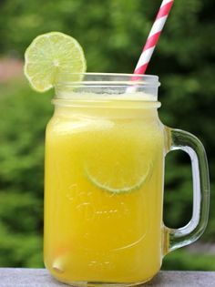 a mason jar filled with yellow liquid and a striped straw next to a lime slice