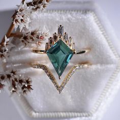 a ring with an emerald colored stone surrounded by white flowers