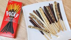 some sticks are on a white plate and next to a box of pockys