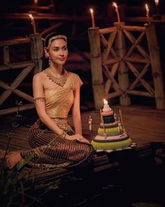 a woman sitting next to a cake on top of a wooden table with candles in the background