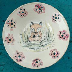 a plate with an image of a fox sitting in the grass and flowers on it