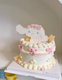 a white cake with pink flowers and an elephant on top is sitting on a shelf