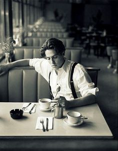 a man sitting at a table in front of a cup and saucer with spoons