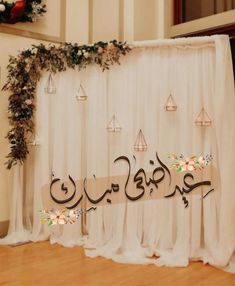 an arabic calligraphy is displayed in front of a backdrop with hanging candles and flowers