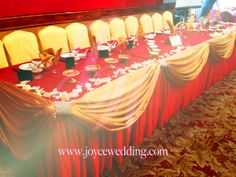 a long table with red cloths and gold chairs is set up for an event