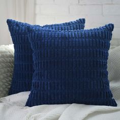 two blue pillows sitting on top of a bed next to each other in front of a white brick wall