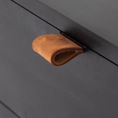 a piece of brown leather hanging on the side of a black cabinet door with a wooden handle