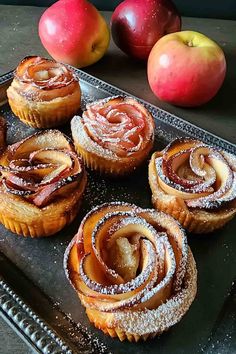 several pastries on a tray with apples in the background