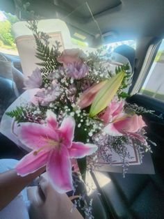 a bouquet of pink flowers in the back seat of a car with someone's hand holding it