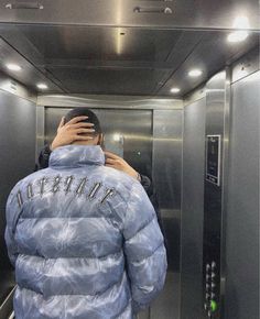 a person in a blue jacket taking a selfie with his cell phone while standing inside an elevator