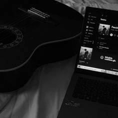 an open laptop computer sitting on top of a bed next to a guitar and keyboard