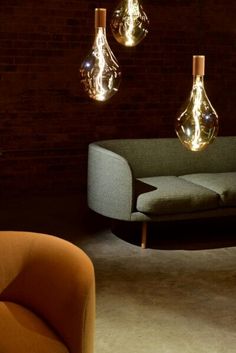 three light bulbs hanging from the ceiling above a couch and chair in a dark room