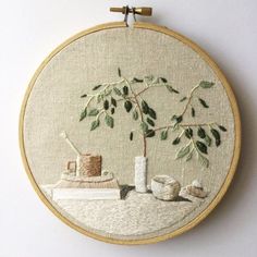 an embroidered wall hanging with a potted plant and coffee mug on the table next to it