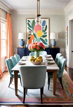 a dining room table with blue chairs and an art work on the wall behind it