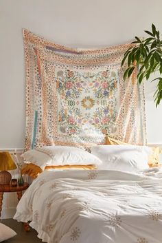 a white bed topped with pillows and blankets next to a potted plant on top of a wooden table