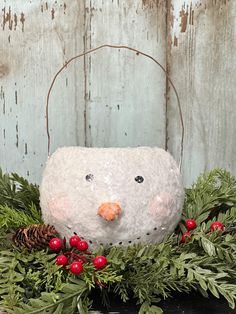 a snowman made out of rock sitting on top of evergreen leaves and red berries