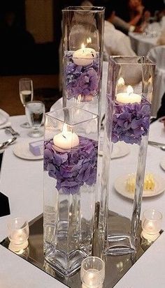 three tall clear vases filled with flowers and lit candles on top of a table