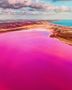 pink lake surrounded by mountains and clouds in the sky with water below it, from above