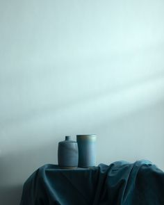 two vases sitting on top of a table covered by a blue cloth in front of a white wall