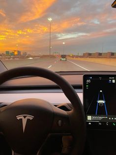 the dashboard of a car with an electronic device on it's dash board, in front of a cityscape at sunset