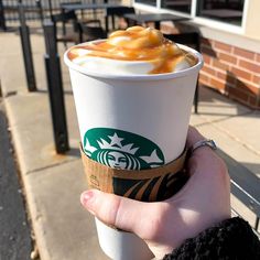 a person holding up a starbucks cup with caramel on top and whipped cream in it