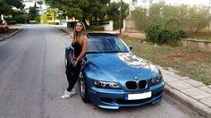 a woman leaning on the hood of a blue car