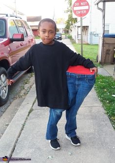 a young boy standing on the sidewalk with his hands in his pockets while leaning against a sign that says do not enter